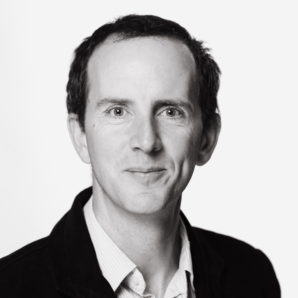 Black and white portrait picture of John Fingleton smiling slightly.